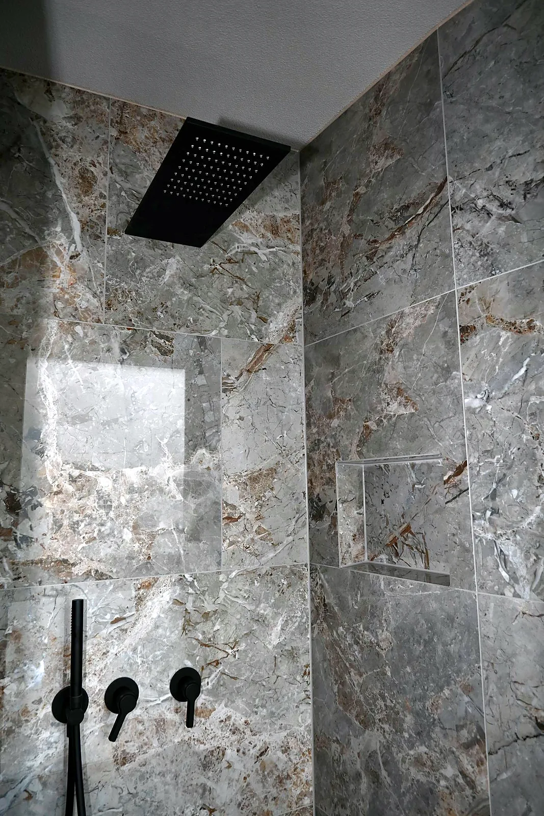 Dusche mit schwarzem Regenpaneel und Nische in grauer Marmoroptik